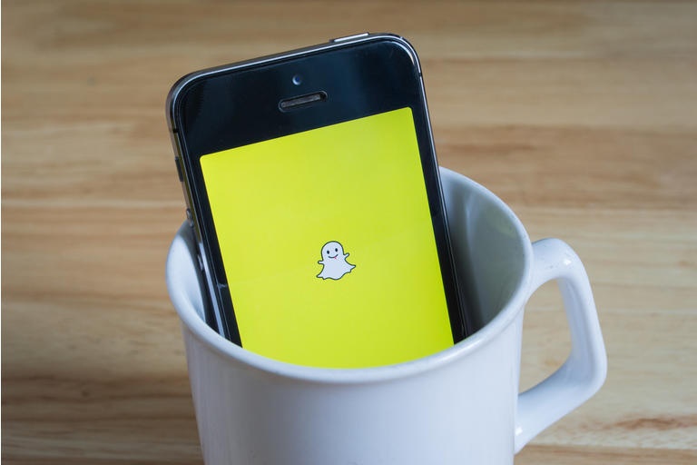 Apple iPhone5s in a mug showing its screen with Snapchat logo.